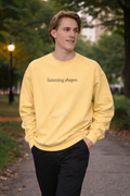 Person wearing a yellow sweatshirt with 'listening shapes' text, standing outdoors.