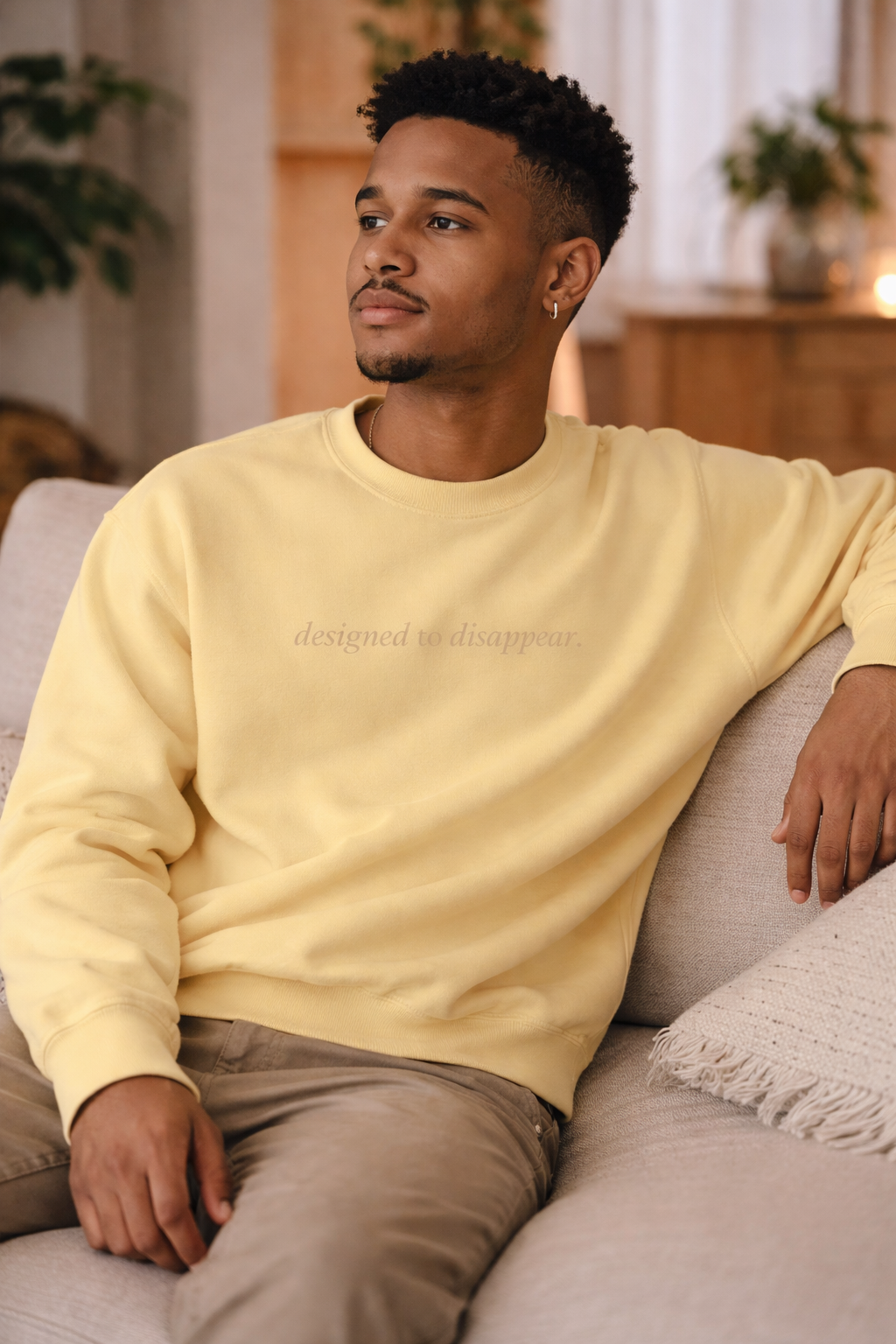 Man wearing a light yellow sweatshirt sitting on a couch in a living room.