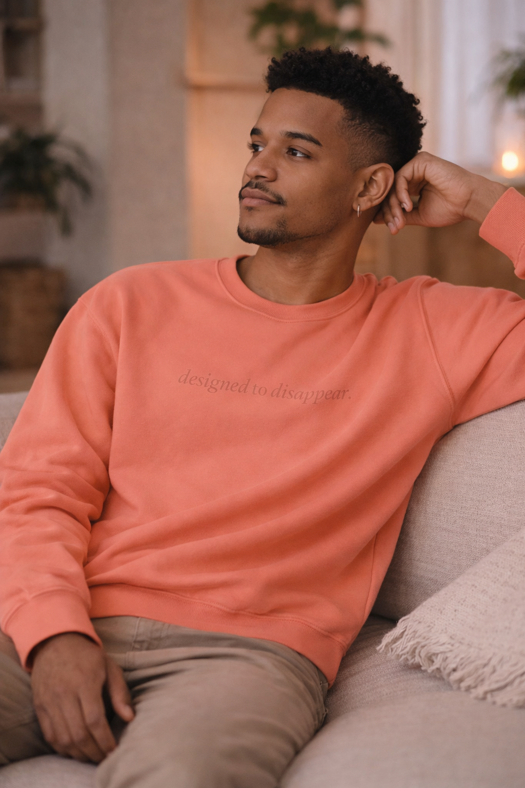 Man wearing a peach-colored sweatshirt sitting on a couch in a cozy living room.