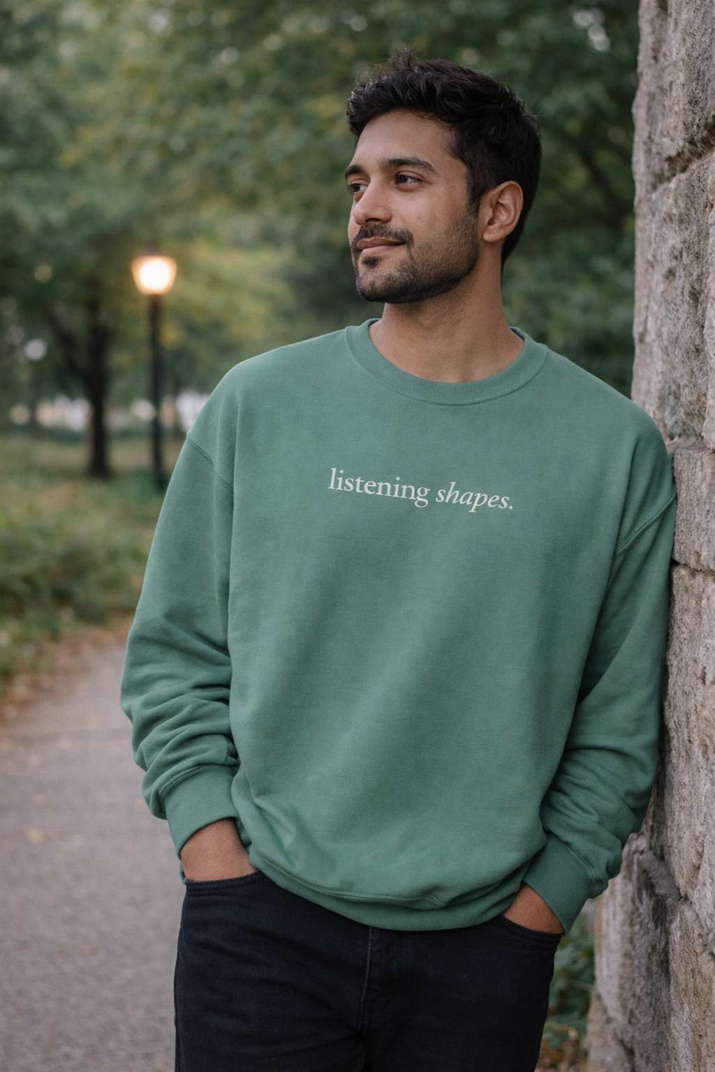 Man wearing a green sweatshirt with 'listening shapes' text, standing outdoors.