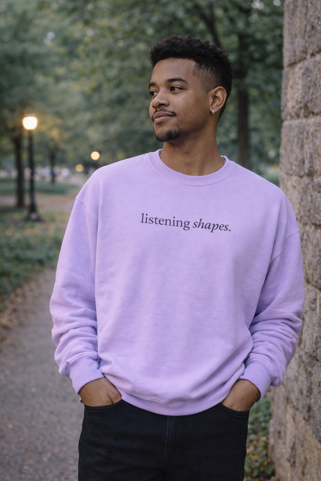 Man wearing a purple sweatshirt with text, standing outdoors near a stone wall.